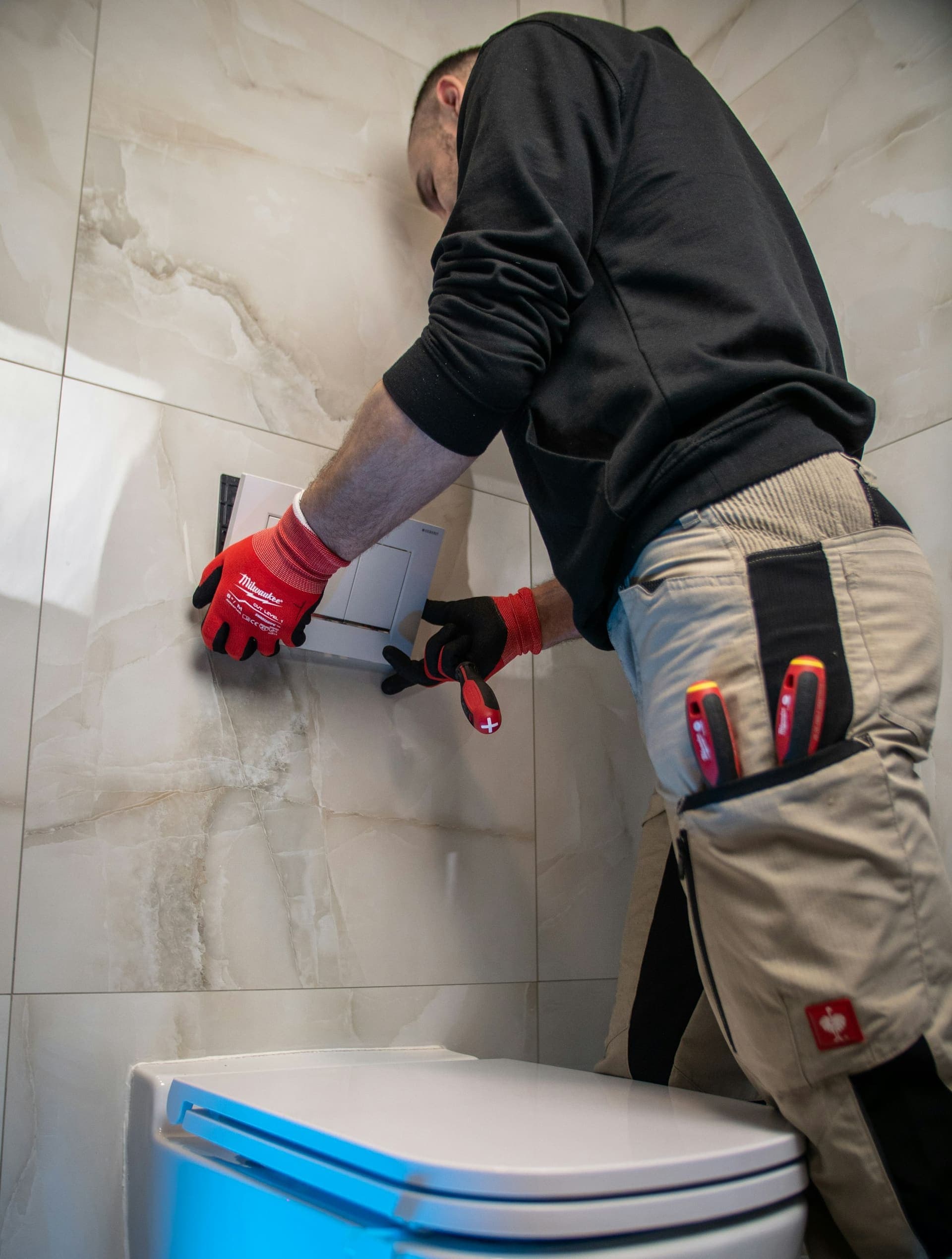 Loodgieter monteert een bedieningsplaat van een inbouwtoilet